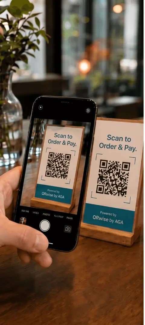 A guest pointing a phone camera at a QRwise table card on a wooden café table